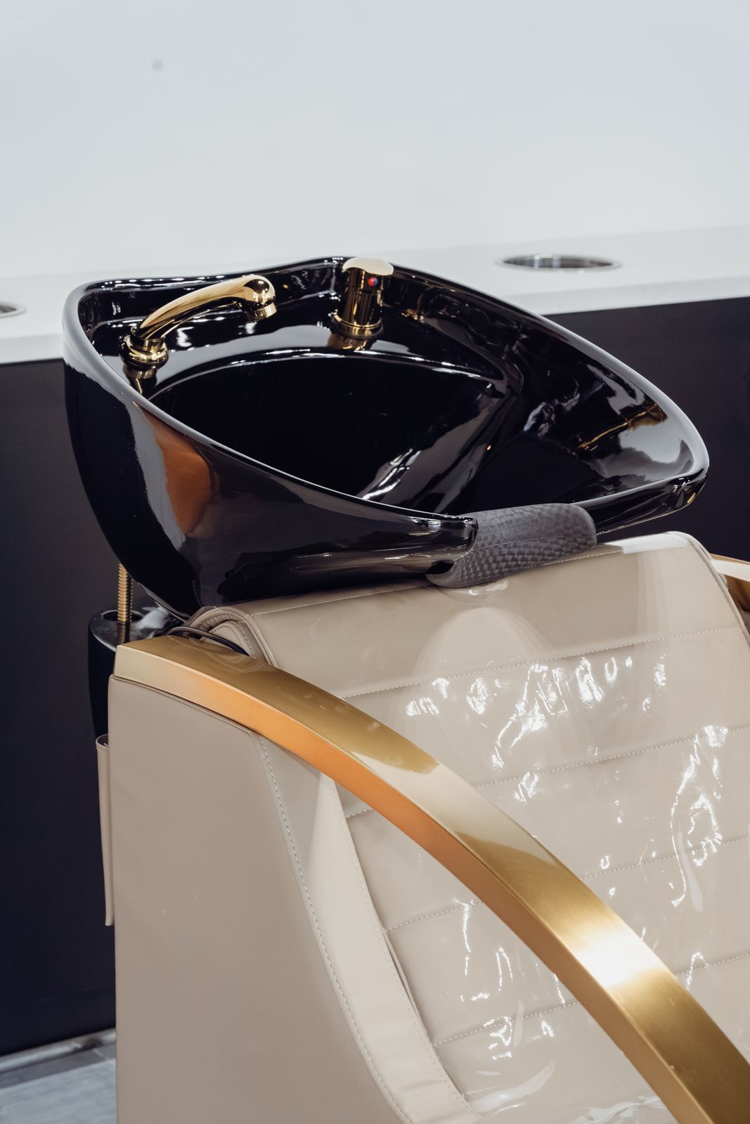 Black shampoo basin with gold fixtures and a cream salon chair