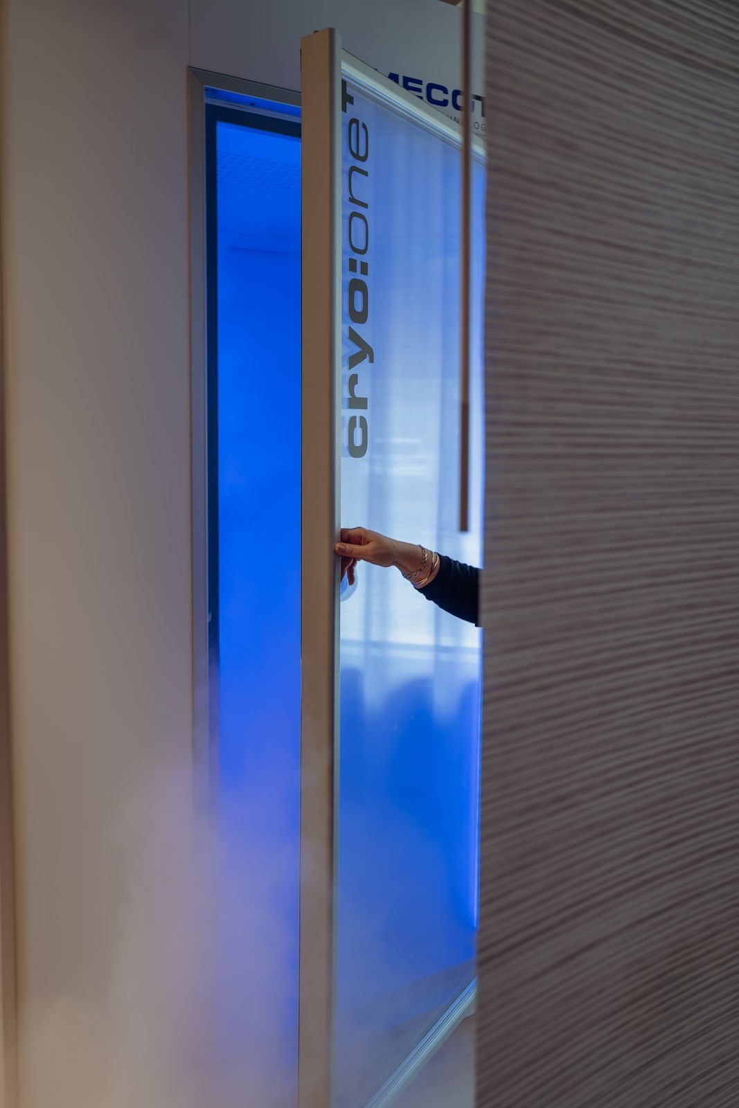 Hand opening the cryotherapy chamber door as cold mist escapes