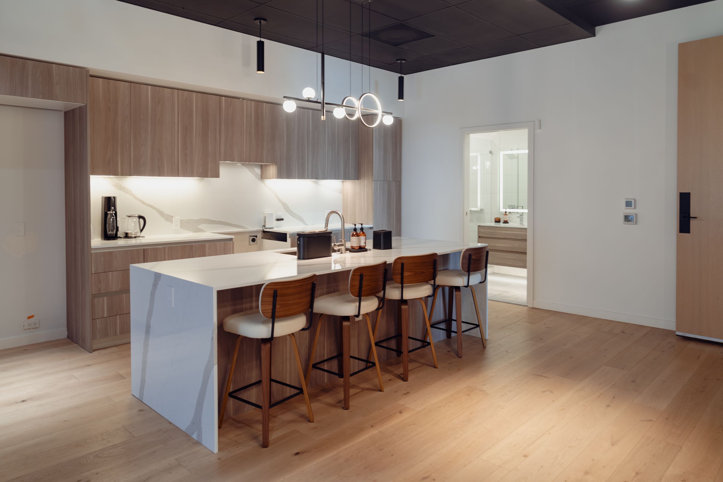 Guest lounge with a marble waterfall island, walnut stools and pendant lighting